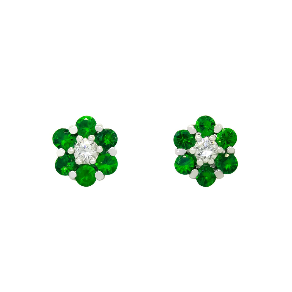 A product photo of a pair of tsavorite and diamond stud earrings in 9k white gold sitting on a white background. Each earring consists of 6 little tsavorite stones arranged around a single diamond centre-stone in a floral-like pattern. The tsavorites reflect electric green hues across their multi-faceted edges.