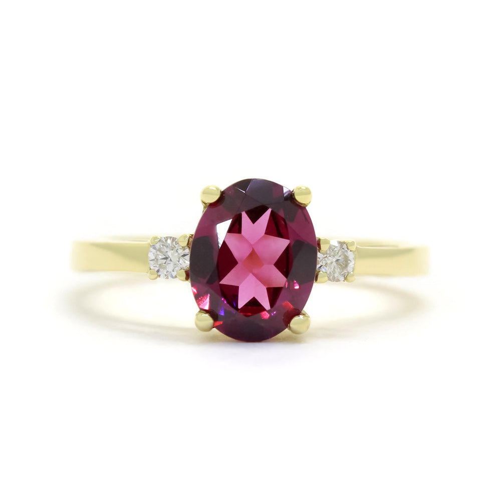 A product photo of a dainty and elegant yellow gold ring with a stunning trio of rhodalite and diamonds sitting against a white background. The largest of the stones sits in the centre, an oval rhodalite - hugged by two smaller circular white diamonds on either side.