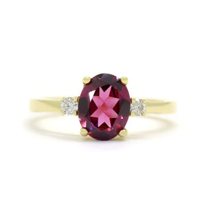 A product photo of a dainty and elegant yellow gold ring with a stunning trio of rhodalite and diamonds sitting against a white background. The largest of the stones sits in the centre, an oval rhodalite - hugged by two smaller circular white diamonds on either side.