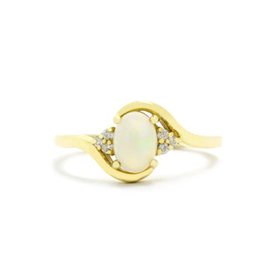 A product photo of a mystical white opal and diamond fantasy ring in solid 9k yellow gold on a white background. The fiery white opal is held in place by 4 claws and reflects light off of its many facets, while 3 diamonds sit on either side.. The smooth yellow gold band curves elegantly, meeting at the top and bottom of the opal and diamond arrangement.