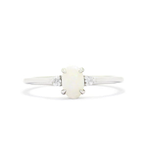 A product photo of a delicate 9ct white gold 6x4mm white opal and diamond trio ring sitting on a white background. The fiery opalite centre stone is hugged on either side by a bright white diamond jewel.