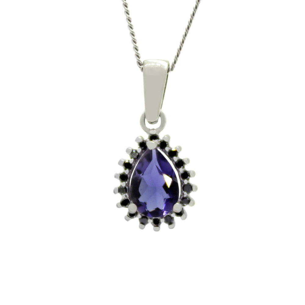A product photo of a lavishly ornate iolite pendant bejewelled with a black diamond halo in solid 9ct white gold suspended by a golden chain against a white background. The large pear-shaped midnight blue gemstone is oval-shaped, and is surrounded by a star-like halo of white gold and black diamond details. The dark blue colour could make it a good sapphire or tanzanite alternative.