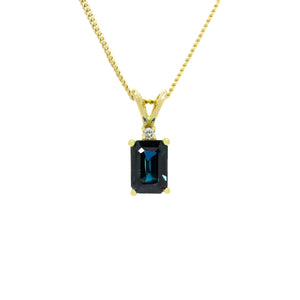 A product photo of a rectangular sapphire and diamond pendant in 9k yellow gold suspended against a white background. The rectangular, emerald-cut sapphire is a stunningly deep ocean blue colour. A single white diamond sits atop it, before meeting the split golden bail.