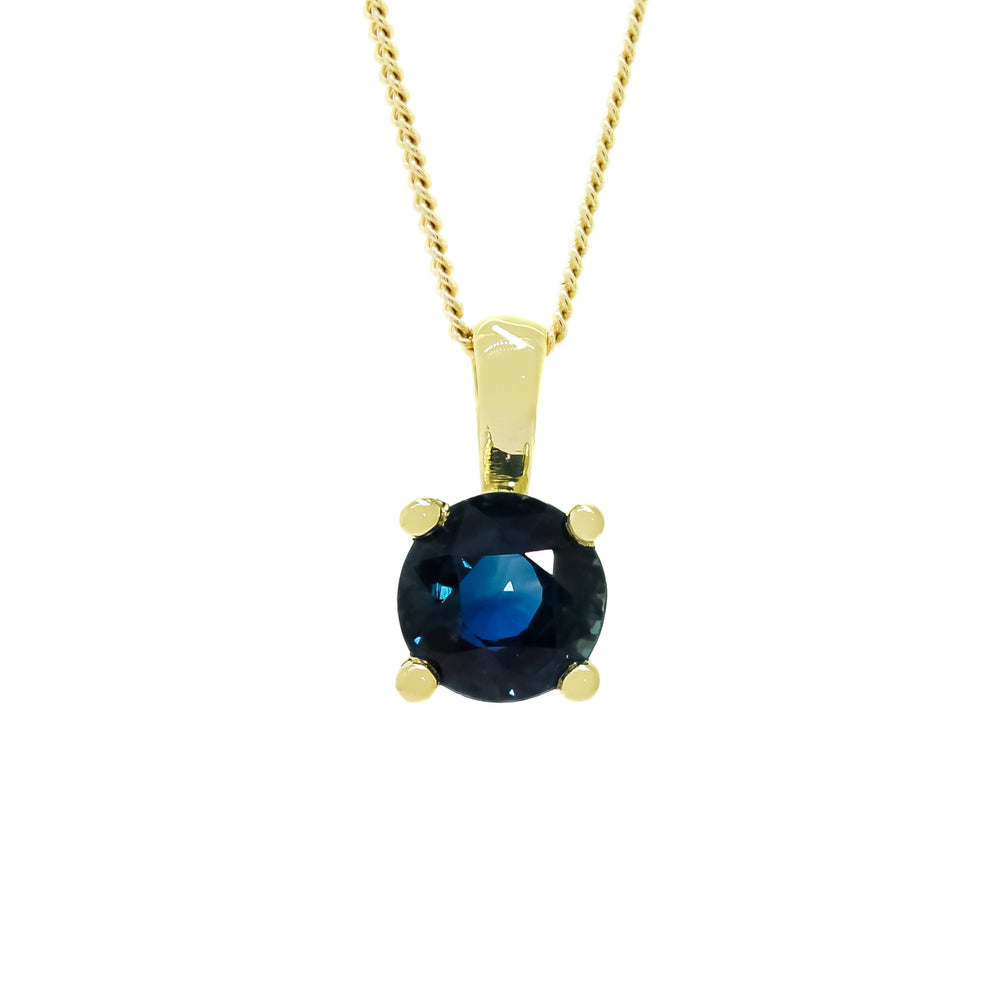 A product photo of a 9ct yellow gold fine sapphire pendant suspended by a gold chain against a white background. The round stone is held in place by 4 small claws, and reflects ocean blue hues from its many edges.