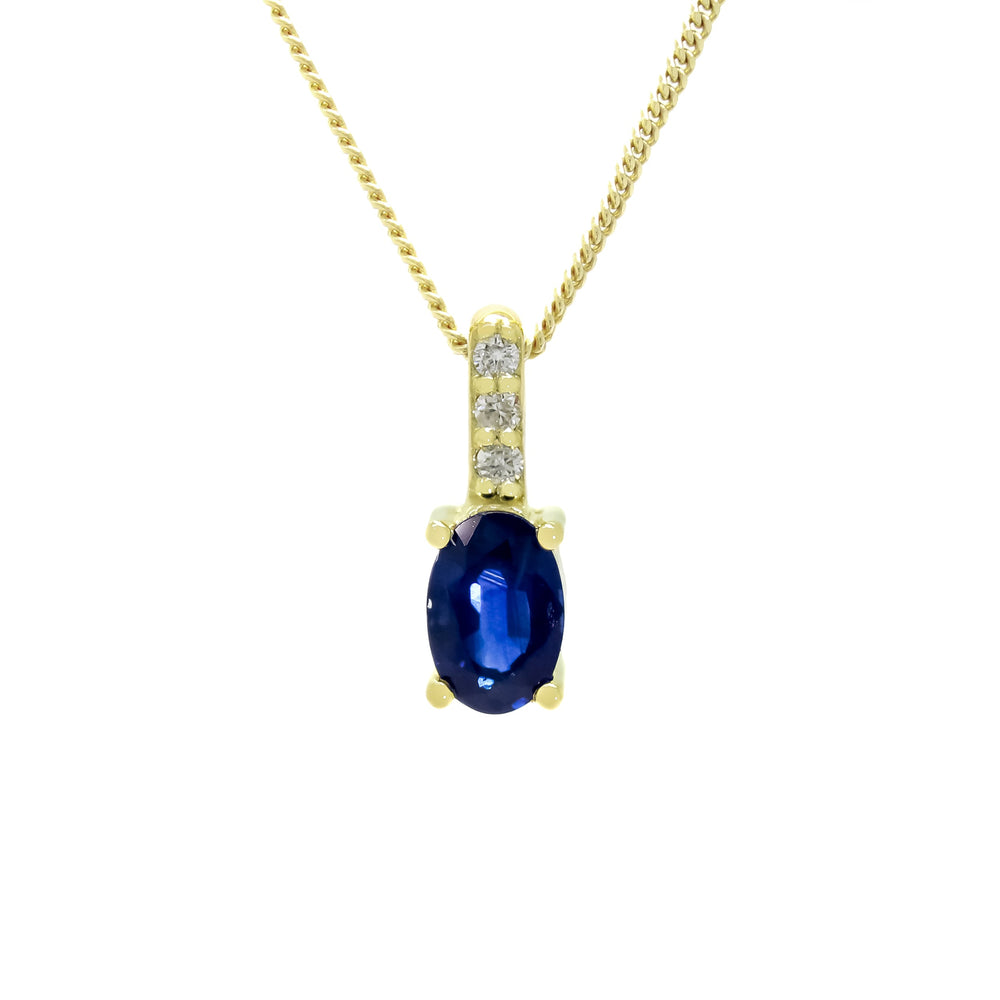 
            
                Load image into Gallery viewer, A product photo of a yellow gold sapphire pendant suspended against a white background. The simple oval-cut stone is contrasted by the white diamond trio protruding in a straight line above the magenta ruby, encased in yellow gold.
            
        