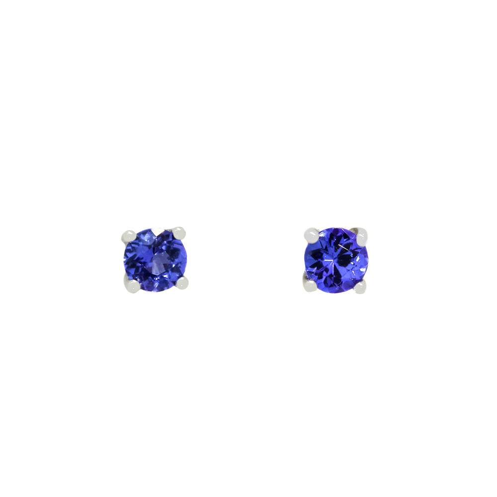 
            
                Load image into Gallery viewer, A product photo of two white gold stud earrings sitting on a white background. Held in place by 4 silver claws each are two dazzling round-cut indigo blue tanzanite gemstones, reflecting shades of cool violet from their many edges.
            
        