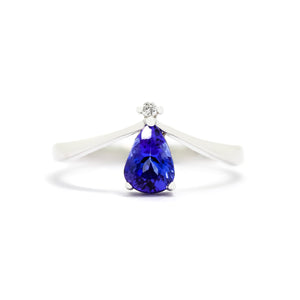 A product photo of a delicate tanzanite teardrop ring with a single diamond accent in 9ct white gold sitting on a white background. The smooth, slim white gold band curves elegantly to meet a tiny, 0.015ct white diamond jewel, which sits atop a 7x5mm pear shaped indigo blue tanzanite gemstone.