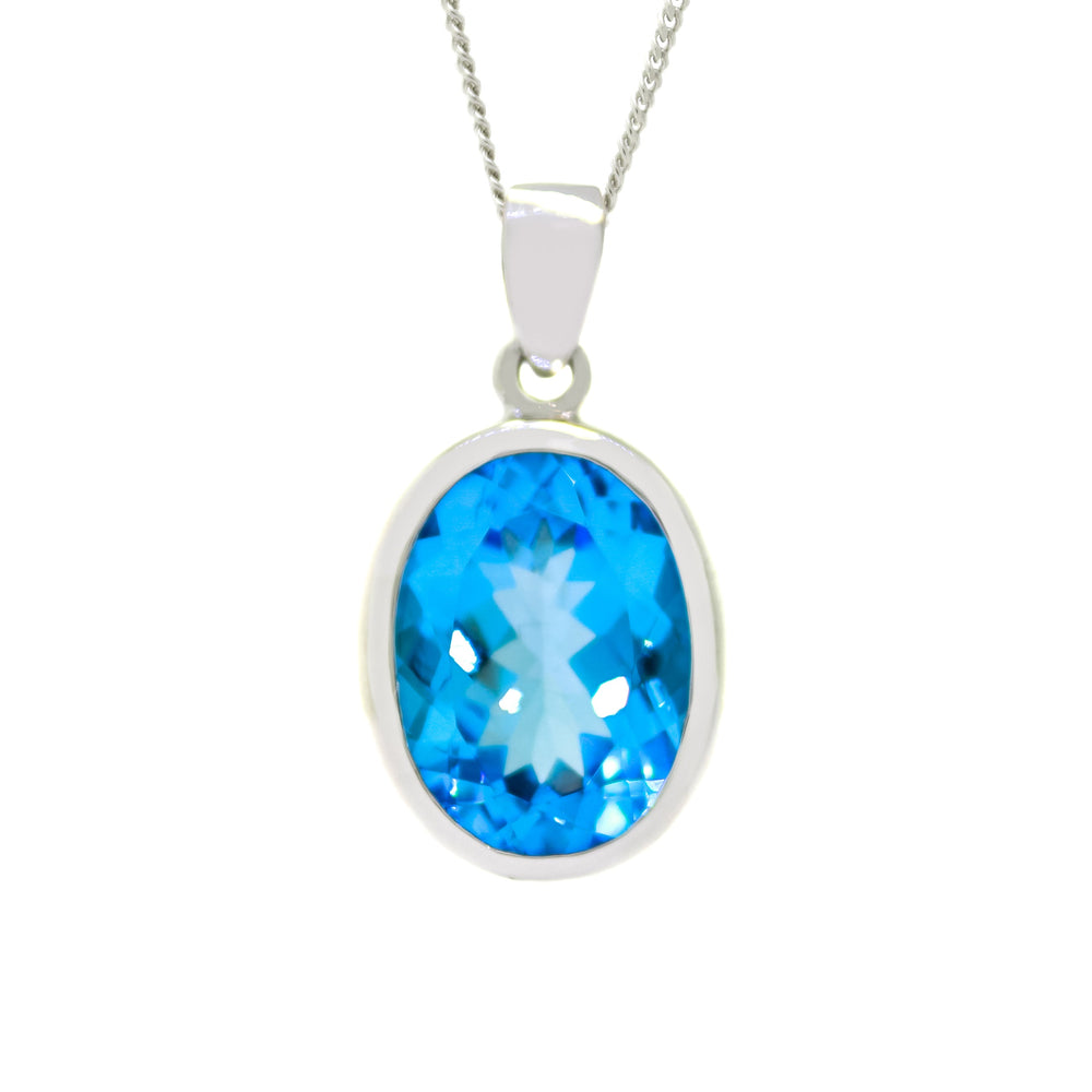 A product photo of a massive oval blue topaz pendant in a silver bezel setting sitting on a white background. The stone measures 12x16mm.