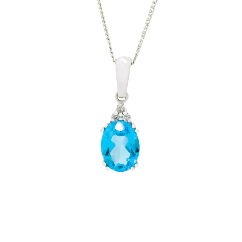 
            
                Load image into Gallery viewer, A product photo of a white gold blue topaz necklace sitting against a white background. The light blue oval-cut stone is held in place by 4 pairs of claws at its top and bottom, with a trio of white diamonds connecting the stone to the rest of the pendant. It is suspended by a simple white gold chain.
            
        