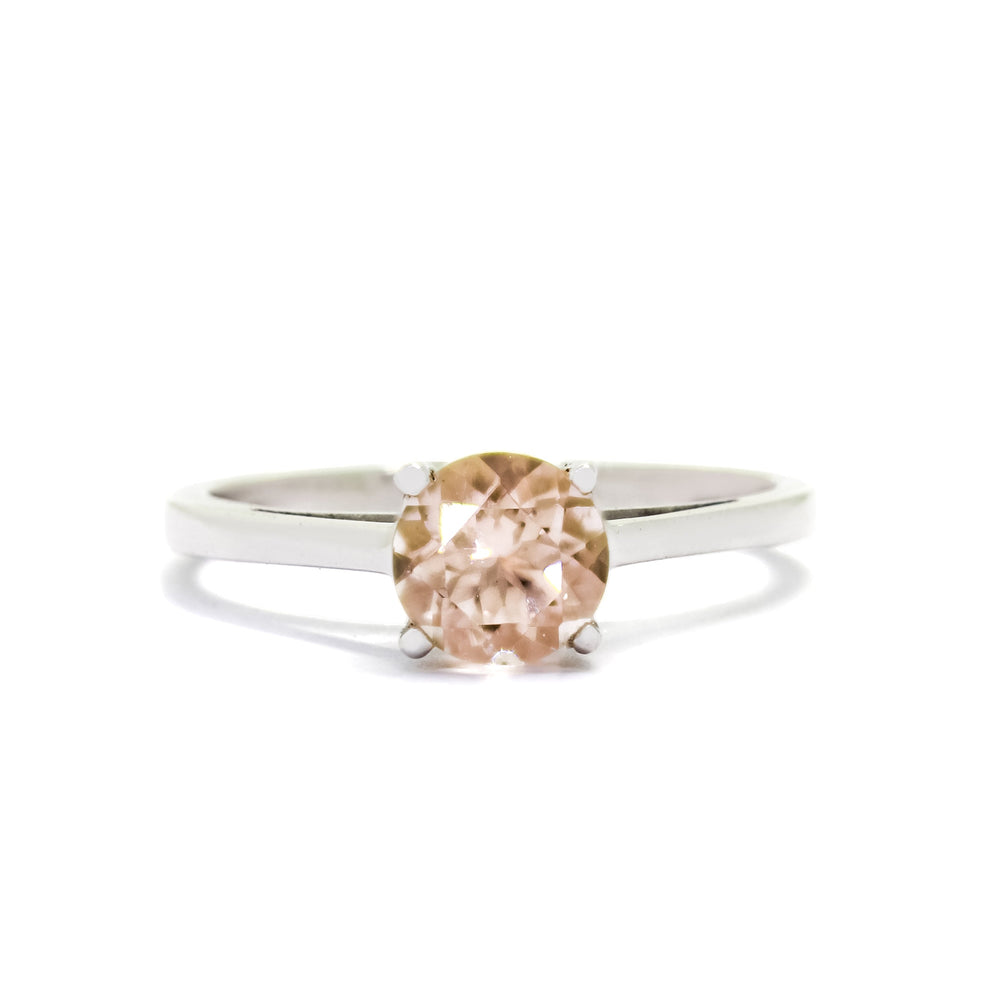 A product photo of a simple morganite solitare ring set in solid 9k white gold sitting on a white background. The face of the ring is deceptively simple, appearing like a standard solitare ring, but with hidden cathedral style supports and a stylised floral backing connecting the stone to the band.