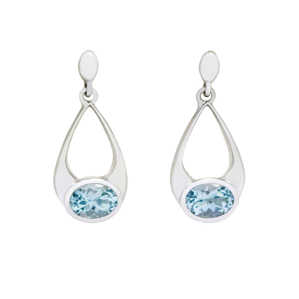A product photo of a pair of solid 9 karat white gold aquamarine earrings. The 7x5mm oval aquamarine stones are horizontally-oriented and encased in a bezel setting, each situated at the base of bold, teardrop-shaped golden frames.