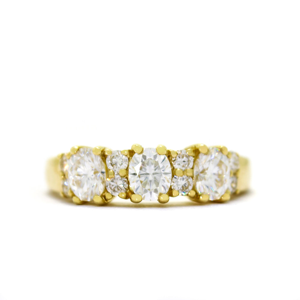 A product photo of a bold and lavish moissanite and diamond ring in 9k yellow gold. The ring is made up of three large oval moissanite stones, while 2 diamonds fill the spaces between and on either side of the moissanites- to a total of 0.32ct for 8 diamonds.
