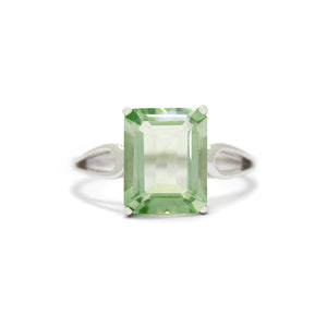 A product photo of a green amethyst ring in 9 karat white gold sitting on a white background. The ring consists of a large, vertically-oriented rectangular centre stone, held in place by delicate golden loops in the band on either side. The jewel is a delicate pale green.