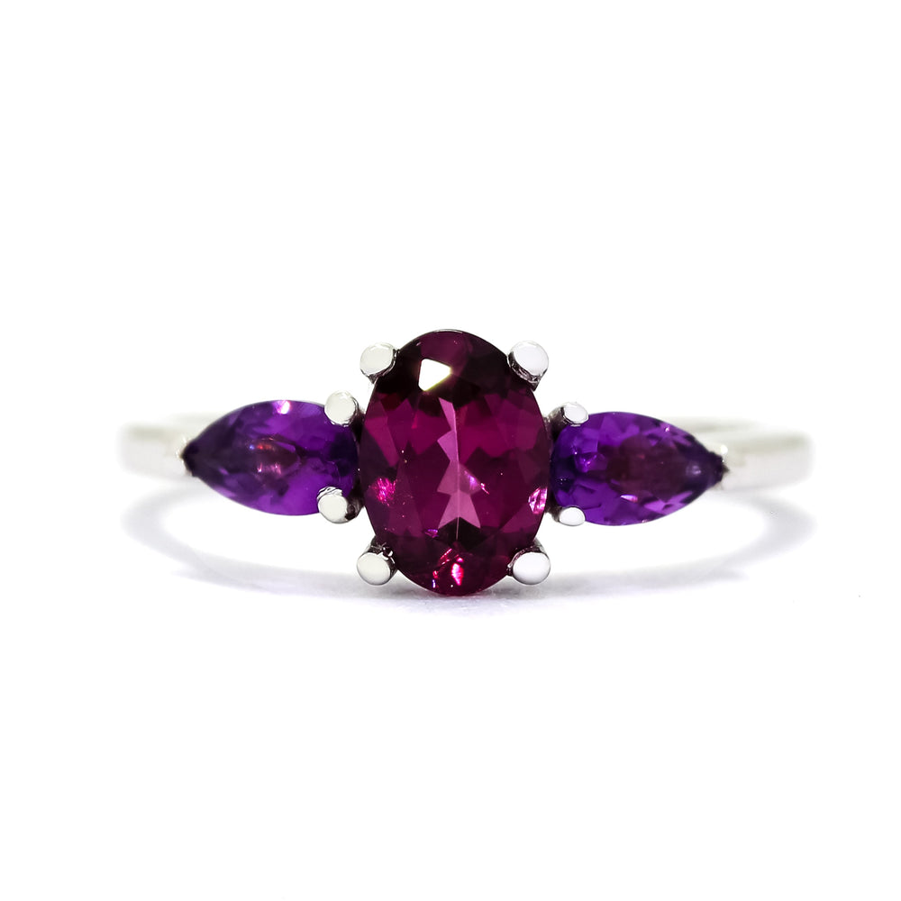 A product photo of a dainty and elegant white gold ring with a stunning trio of grape garnet and amethysts sitting against a white background. The largest of the stones sits in the centre, a 7x5mm oval grape garnet - hugged by two smaller pear-shaped amethyst stones on either side.