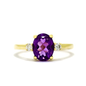 
            
                Load image into Gallery viewer, A product photo of a dainty and elegant yellow gold ring with a stunning trio of amethyst and diamonds sitting against a white background. The largest of the stones sits in the centre, an oval amethyst - hugged by two smaller circular white diamonds on either side.
            
        