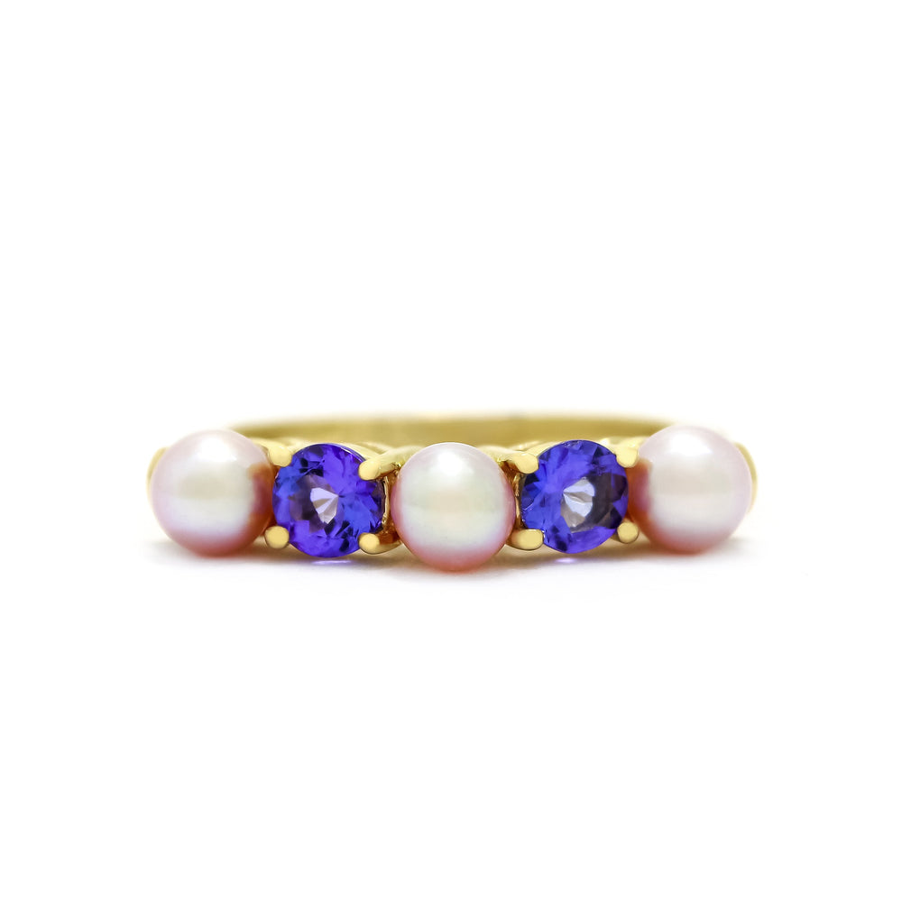 This product image shows a rosaline pearl and tanzanite eternity ring set in solid 9 karat yellow gold. The ring is made up of 3 round pale pink rosaline pearls of 4.5mm in diameter, two on the outer edges of the eternity design and one in the centre. Between each pearl sits an electric blue round-cut tsavorite jewel of similar sizing.