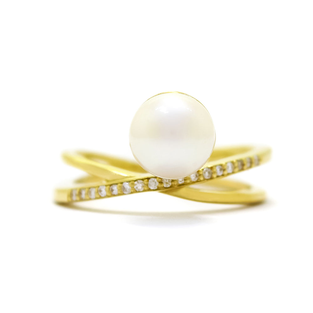 This product image shows an asymmetrical pearl and diamond ring design set in solid 9 karat yellow gold. The ring is made up of two slim bands, each tilted at a slight angle, only intersecting in the centre of the ring. The one that crosses over in the front is embedded with diamonds along the band, while the other band is smooth. The pearl is set slightly higher up on the diamond-embedded band instead of where they intersect - creating an interesting off-centre effect.