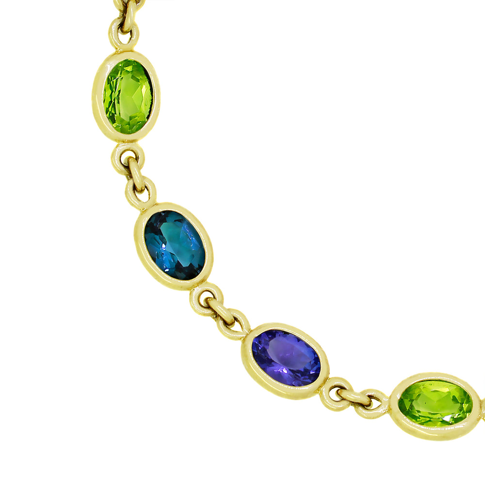 A product photo of a 9 karat yellow gold bracelet made up of 12 7x5mm oval-shaped London Blue Topaz, Tanzanite and Peridot gems in bezel settings sitting on a clear white background.