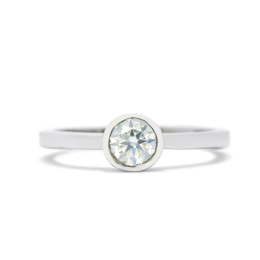 A product photo of a solid 925 sterling silver bezel-set solitaire ring. A single, dazzling white moissanite sits encased in a thick layer of silver framing. The white colouring and multi-coloured refractions would make it a good diamond alternative.