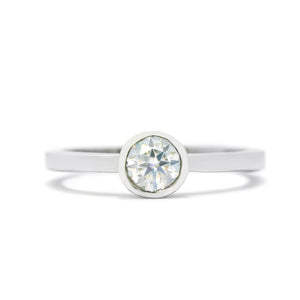 A product photo of a solid 925 sterling silver bezel-set solitaire ring. A single, dazzling white moissanite sits encased in a thick layer of silver framing. The white colouring and multi-coloured refractions would make it a good diamond alternative.
