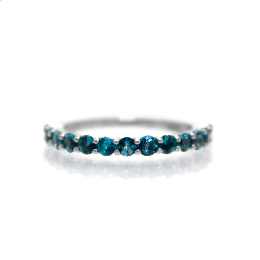 A product photo of a silver eternity band with 13 London Blue Topaz stones embedded along its length on a white background. The deep blue gemstone colour be a good sapphire alternative.