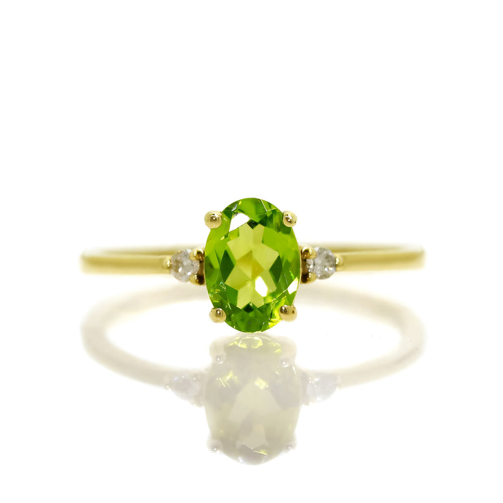 
            
                Load image into Gallery viewer, A product photo of a yellow gold peridot ring sitting against a white background. The yellow gold band is plain and smooth, and the centre oval-cut grass green peridot stone is framed by a single white diamond on either side.
            
        