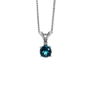 A product photo of a 4.5mm round London Blue Topaz and diamond pendant in 9k white gold suspended against a white background. The delicate topaz gemstone is a stunningly deep ocean blue colour, almost sapphire in appearance. A single white diamond sits atop it, before meeting the split golden bail.