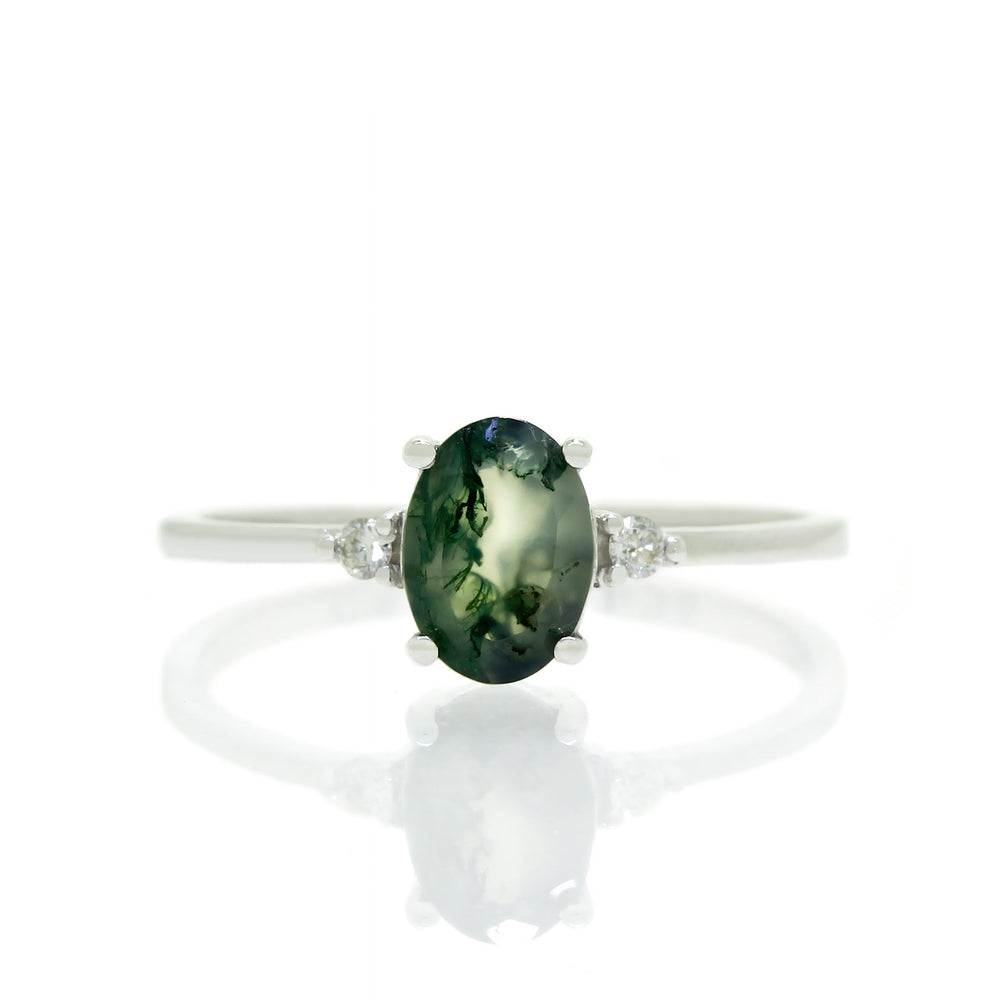 
            
                Load image into Gallery viewer, A product photo of a white gold moss agate ring sitting against a white background. The white gold band is plain and smooth, and the centre oval-cut deep green moss agate quartz stone is framed by a single white diamond on either side.
            
        