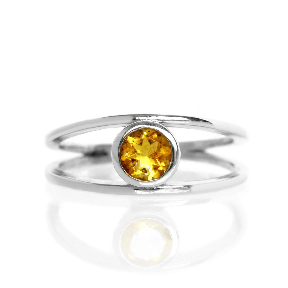 A product photo of a split-band silver ring with a bezel-set citrine centre stone sitting on a white background. The silver band splits at the base of the ring, separating to meet at the top and bottom of the bright orange round-cut centre stone, framed in a thick layer of silver, holding it in place.