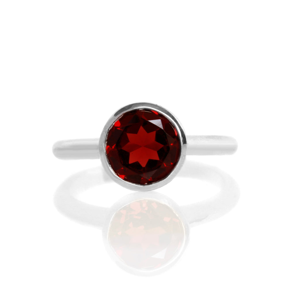 
            
                Load image into Gallery viewer, A product photo of a silver ring with a bezel-set garnet centre stone sitting on a white background. The silver band is simple and smooth, connecting on either side of a large, statement-sized garnet stone surrounded by a solid frame of silver.
            
        