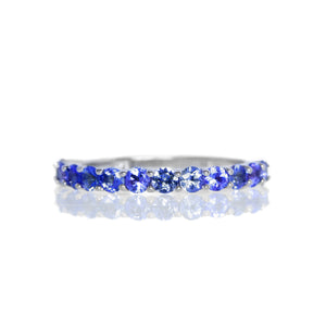 A product photo of a silver eternity band with 13 tanzanite stones embedded along its length on a white background. The deep blue gemstone colour would be a good sapphire alternative.