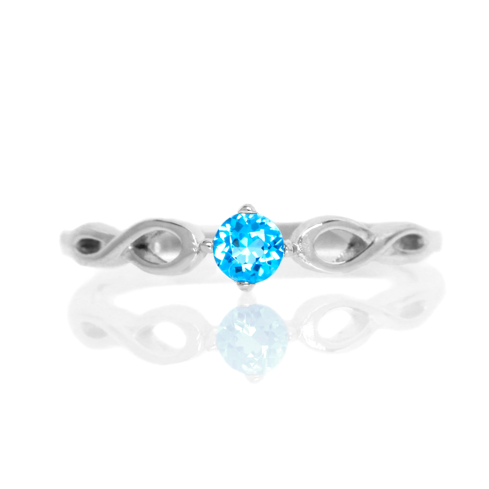 A product photo of an ornate silver ring with a blue topaz centre stone sitting on a white background. The silver band splits halfway along its length, becoming twisting and serpentine in appearance before meeting on either side of the dazzling blue 3.5mm stone, which is held in place by 4 silver claws.