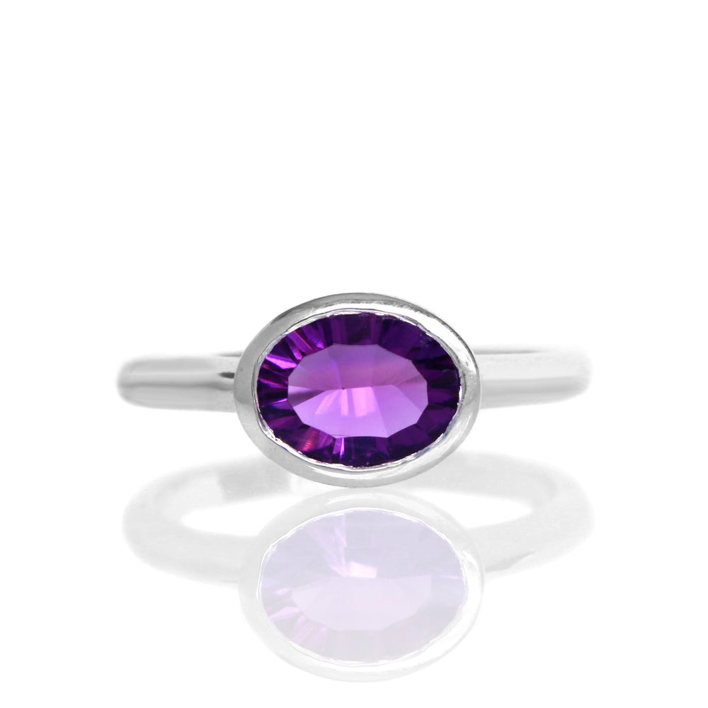 
            
                Load image into Gallery viewer, A product photo of a silver ring with a bezel-set amethyst centre stone sitting on a white background. The silver band is simple and smooth, connecting on either side of a horizontally-oriented oval-cut purple amethyst stone surrounded by a solid frame of silver.
            
        