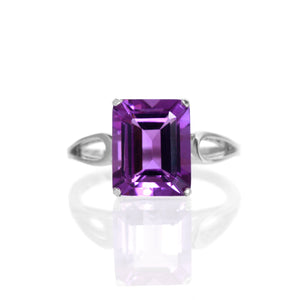 
            
                Load image into Gallery viewer, A product photo of an amethyst ring in silver sitting on a white background. The ring consists of a large, vertically-oriented rectangular centre stone, held in place by delicate silver loops in the band on either side. The jewel is a deep vibrant purple.
            
        