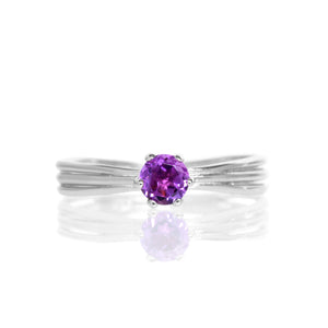 A product photo of a simple silver solitaire ring with a unique band detail and a 4mm round amethyst centre stone sitting on a white background. The band is styled to appear as 3 little silver bands, tilted slightly outwards and "overlapping" towards the back of the ring.