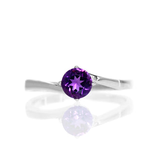 A product photo of a curved-band silver solitaire ring with a deep purple amethyst centre stone sitting on a white background.