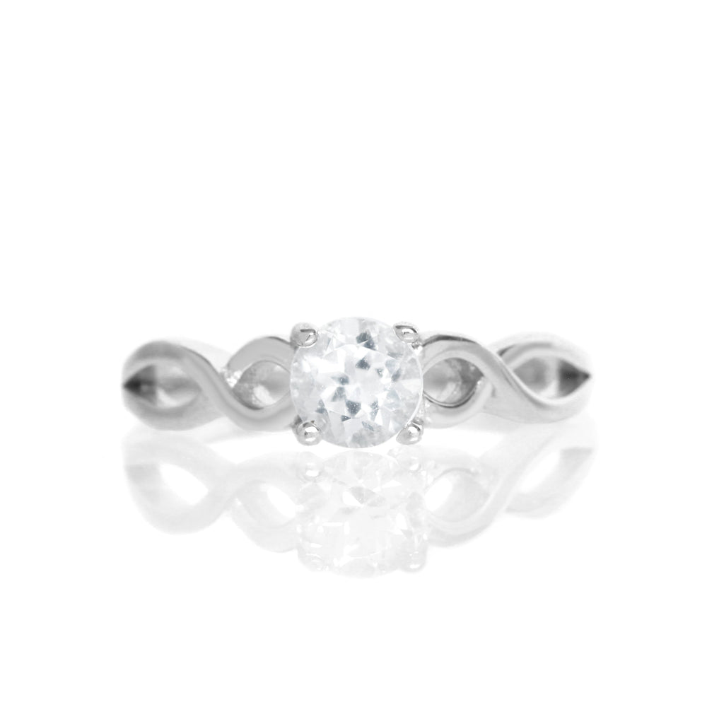 
            
                Load image into Gallery viewer, A product photo of an ornate silver ring with a silver topaz centre stone sitting on a white background. The silver band splits halfway along its length, becoming twisting and serpentine in appearance before meeting on either side of the dazzling white 5mm stone, which is held in place by 4 silver claws.
            
        