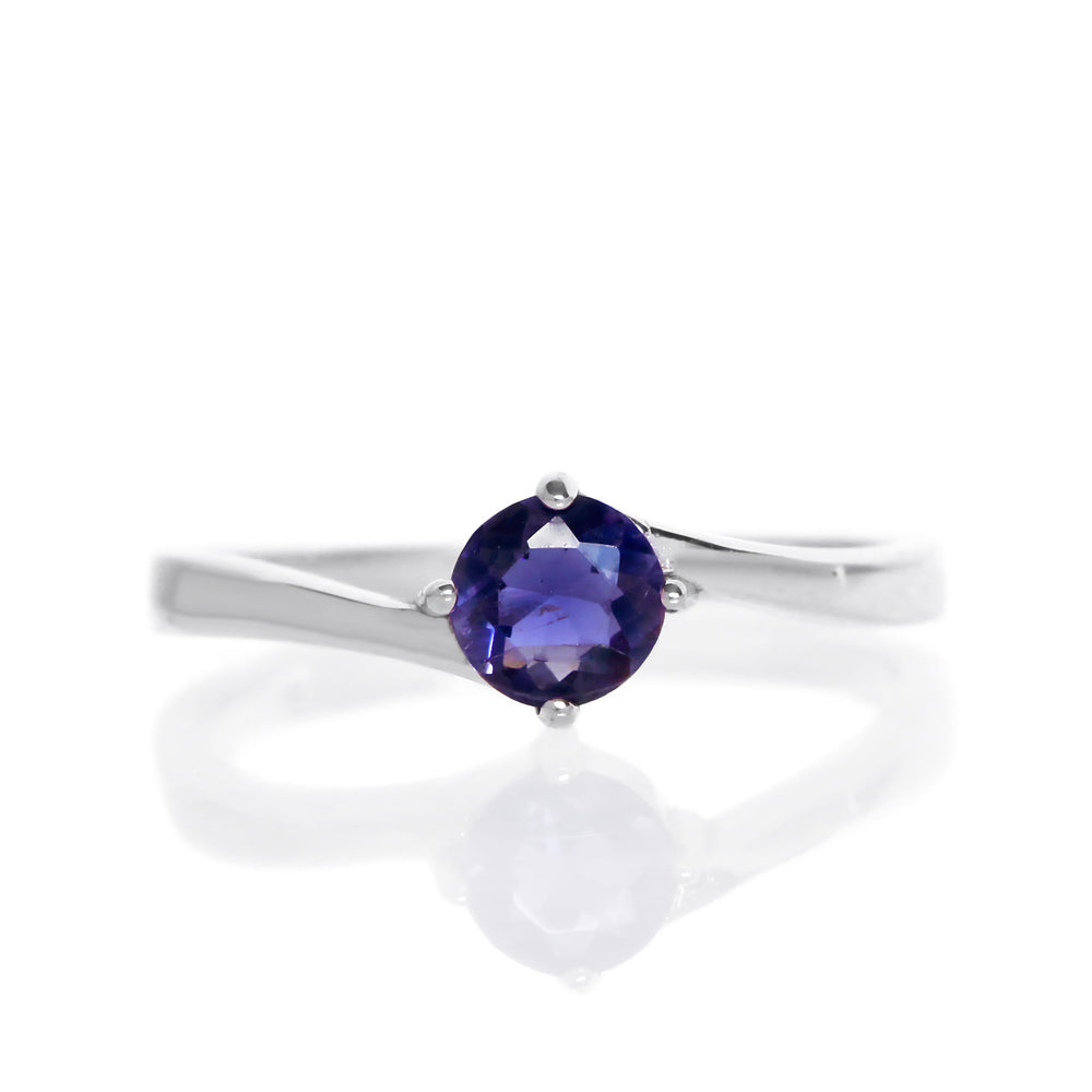 A product photo of a curved-band silver solitaire ring with a midnight blue iolite centre stone sitting on a white background. The deep blue gemstone colour would be a good sapphire substitute.