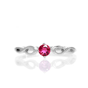 A product photo of an ornate silver ring with a pink tourmaline centre stone sitting on a white background. The silver band splits halfway along its length, becoming twisting and serpentine in appearance before meeting on either side of the dazzling pink 3.5mm stone, which is held in place by 4 silver claws.