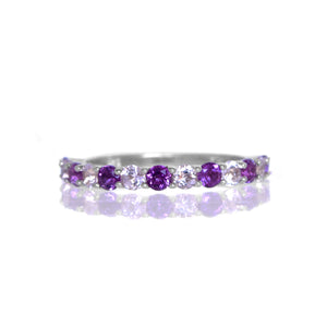 A product photo of a silver eternity band with 13 amethyst and gemstones in alternating order embedded along its length on a white background.
