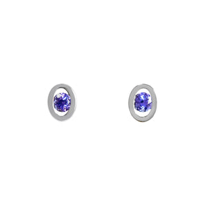 A product photo of a pair of petite tanzanite earrings set in solid 925 sterling silver on a white background. The 3mm tanzanite centre stones are a deep indigo blue. The round stones are held in place by a larger oval frame of silver, giving each earring the appearance of an eye.