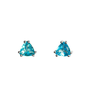 A product photo of a pair of blue topaz stud earrings set in silver on a white background. The blue topaz stones are cut into trilliant shapes, and are held in place by 2 delicate silver claws on either corner.