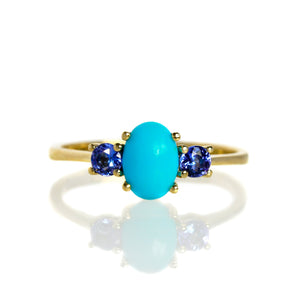 
            
                Load image into Gallery viewer, A product photo of a cabochon Sleeping Beauty turquoise and tanzanite birthstone ring in 9 karat yellow gold on a white background. The 7x5mm turquoise stone is perfectly opaque and unblemished, and is hugged on either side by light blue 3mm round blue topaz jewels.
            
        