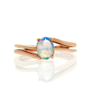 A product photo of an Ethiopian Rainbow Opal ring made of solid 9k rose gold. The opal is uniquely colourful, even compared to other opals - with a mystic blue hue and fierce orange fire throughout. The band is split in two, delicately meeting in the middle in an asymmetrical junction.