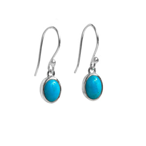 A product photo of a pair of sterling silver turquoise drop earrings suspended against a white background. The drop earrings feature shepherd hooks, and the 8x6mm pear-shaped cabochon turquoise gemstones are held in place by silver bezel settings.