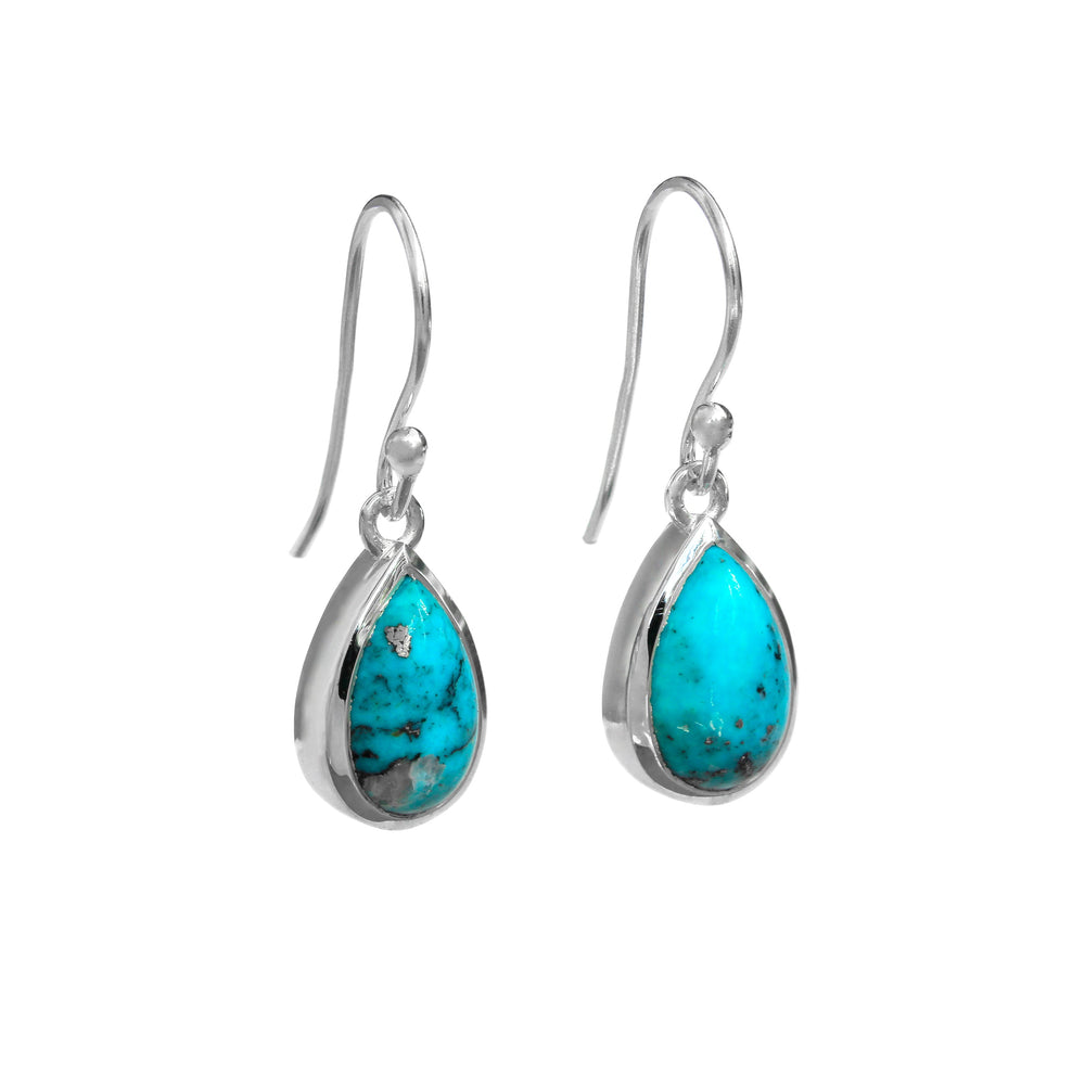 A product photo of a pair of sterling silver Arizonan turquoise drop earrings suspended against a white background. The drop earrings feature shepherd hooks, and the 12x8mm pear-shaped cabochon turquoise gemstones are held in place by silver bezel settings. The stones are decorated by interesting dark natural inclusions.