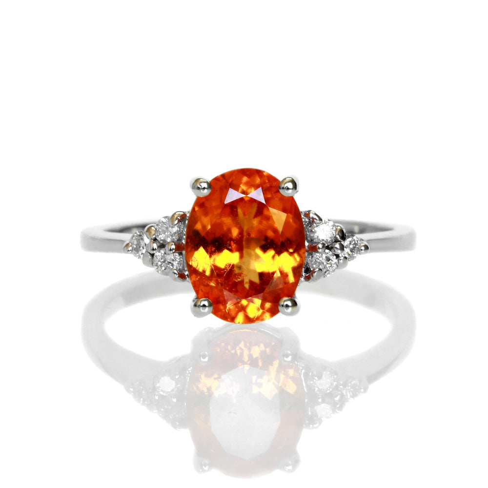 A product photo of an orange mandarin garnet engagement ring in solid 14 karat white gold on a white background. The ring is composed of a 9x7mm electric orange garnet stone, surrounded by 3 delicate white diamonds on either side.