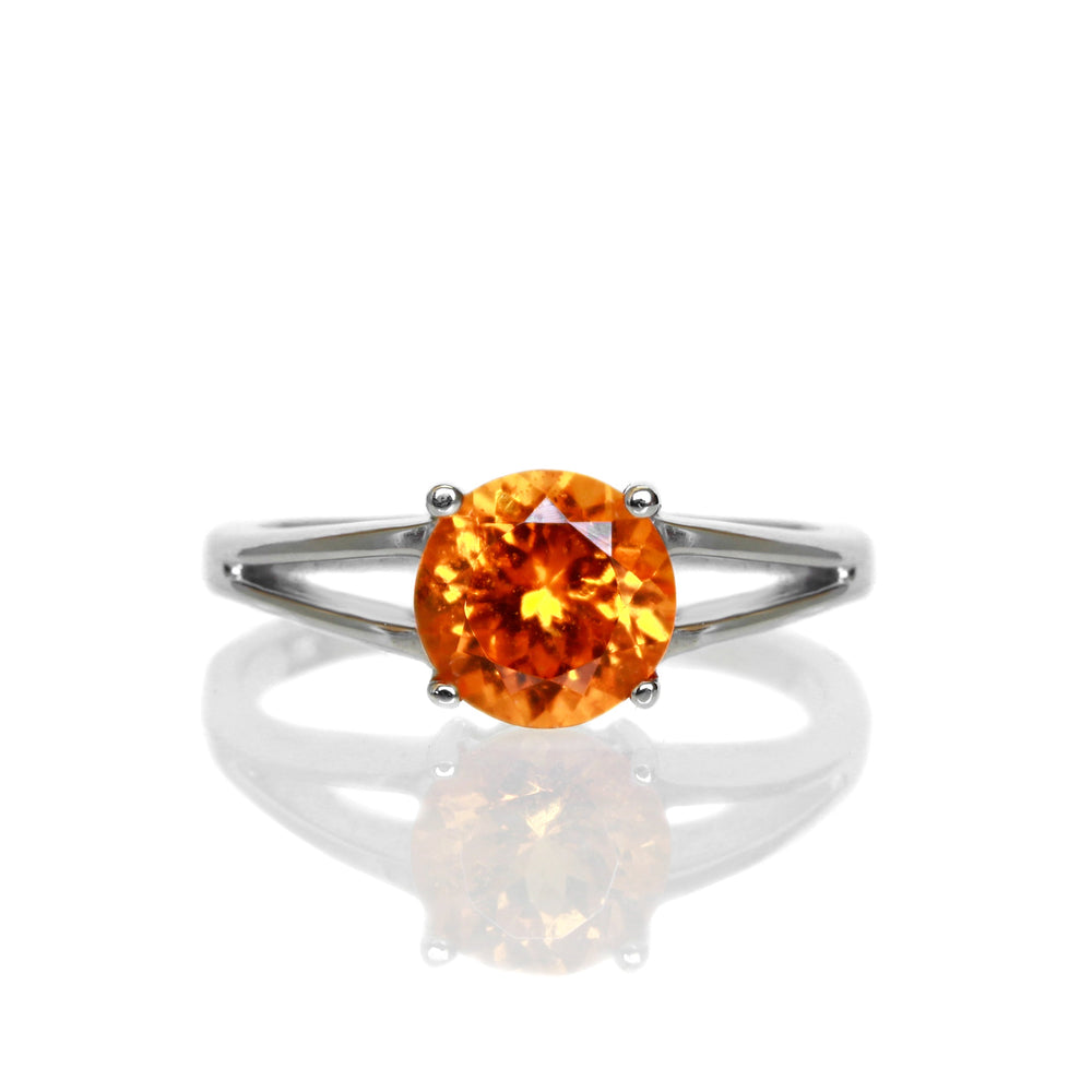 A product photo of an orange mandarin garnet solitaire ring in solid 9 karat white gold on a white background. The band is split into two prongs, meeting on either side of the 7mm round faceted orange garnet jewel.