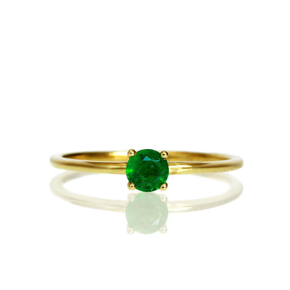 A product photo of a delicate yellow gold stacking ring with a tiny, claw-set emerald in the centre sitting on a white background. The band is slim and thread-like, with the focus drawn to the petite 4mm glinting green emerald gemstone.