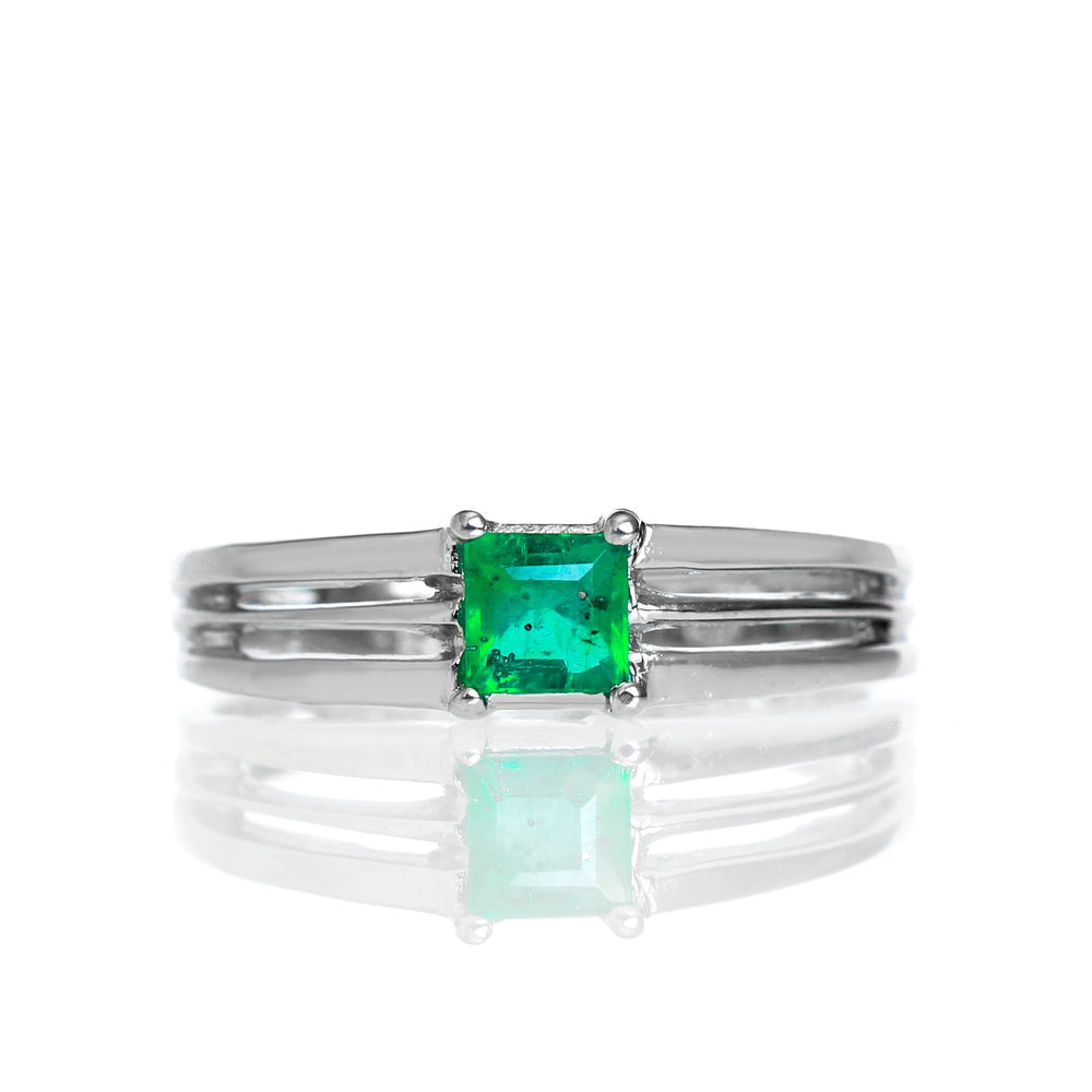 A product photo of a modern emerald ring made of solid 9k white gold sitting on a white background. The 4mm square-shaped emerald is held in place by 3 seperate prongs, splitting apart from the back of the band.